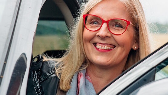 Hymyilev&auml;inen nainen kurkistaa autosta punaiset silm&auml;lasit kasvoilla